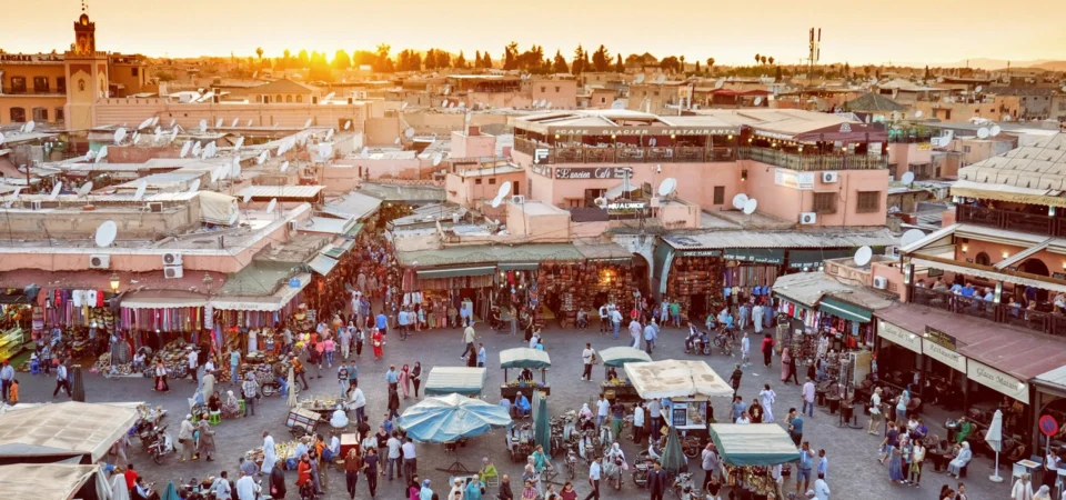 Bustling Jemaa el-Fnaa square in Marrakech during golden hour, filled with market stalls, rooftop cafés, and local crowds.