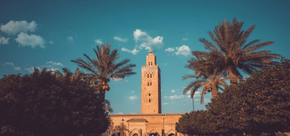 The iconic Koutoubia Mosque in Marrakech, Morocco, framed by palm trees and vibrant gardens under a bright blue sky.
